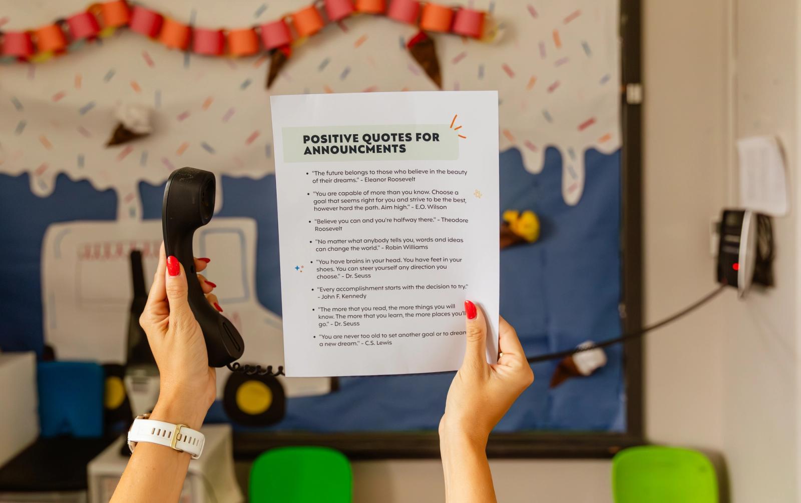 In a classroom, hands hold up a corded phone and a piece of paper. 