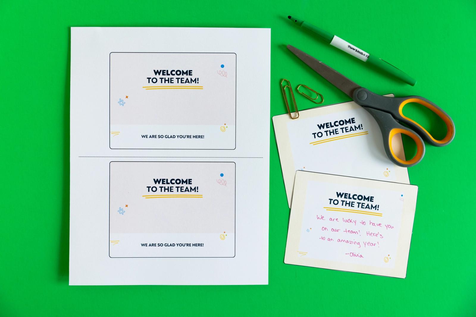 Sheet of paper and two postcards, scissors, and a marker lay on a green background.
