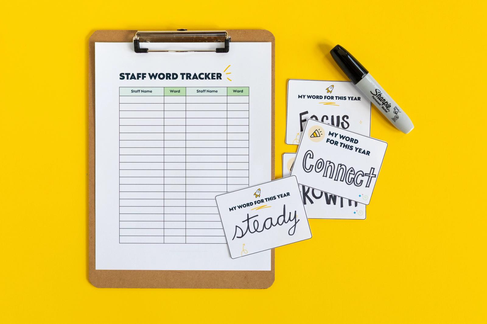 Tracking sheet on clipboard with small notecards with one word written on each. A black marker is beside the clipboard, all on a yellow background.