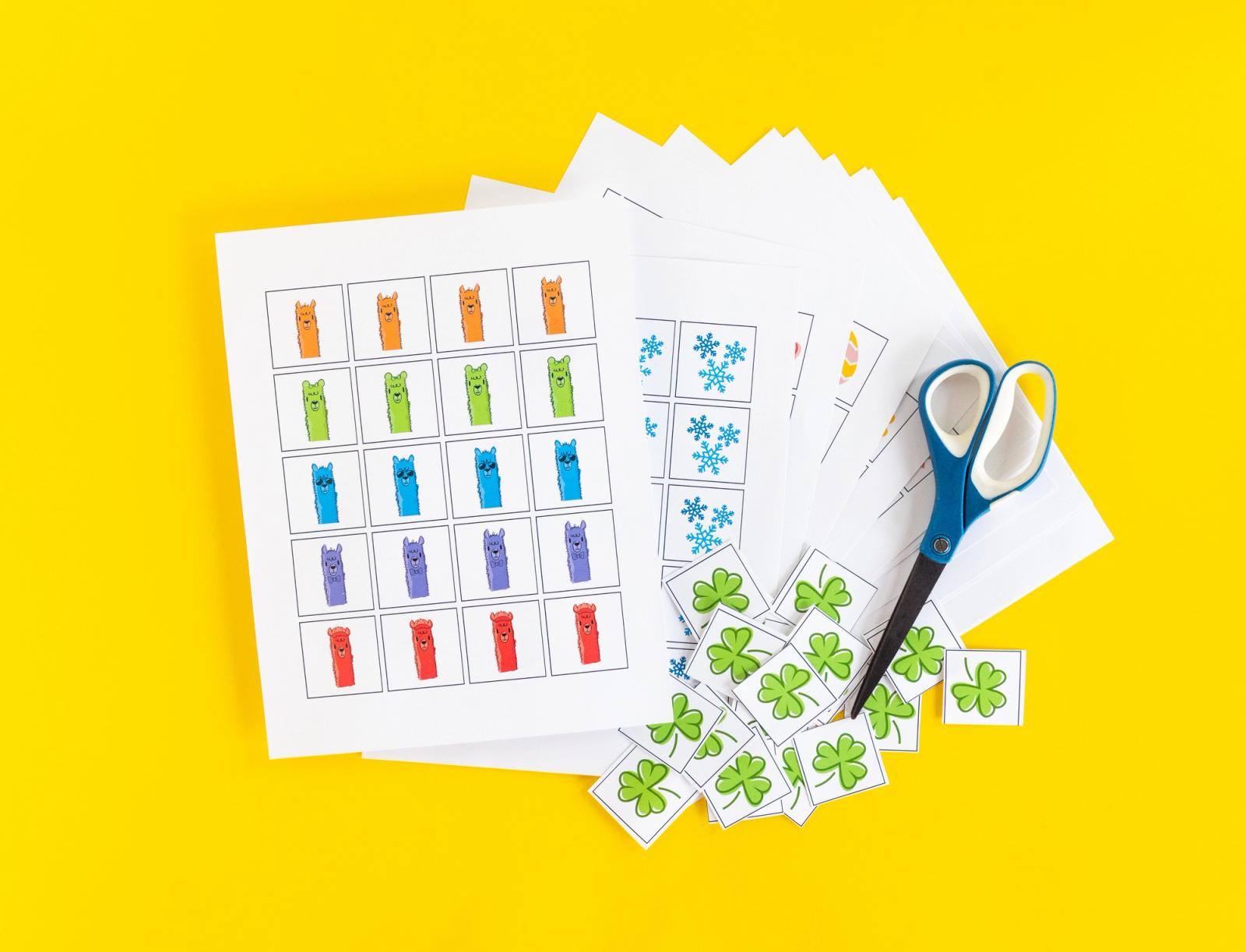 Sheets of paper fanned out with small pictures on them, small pieces of paper with green shamrocks on them, and a pair of scissors lay on a yellow background.