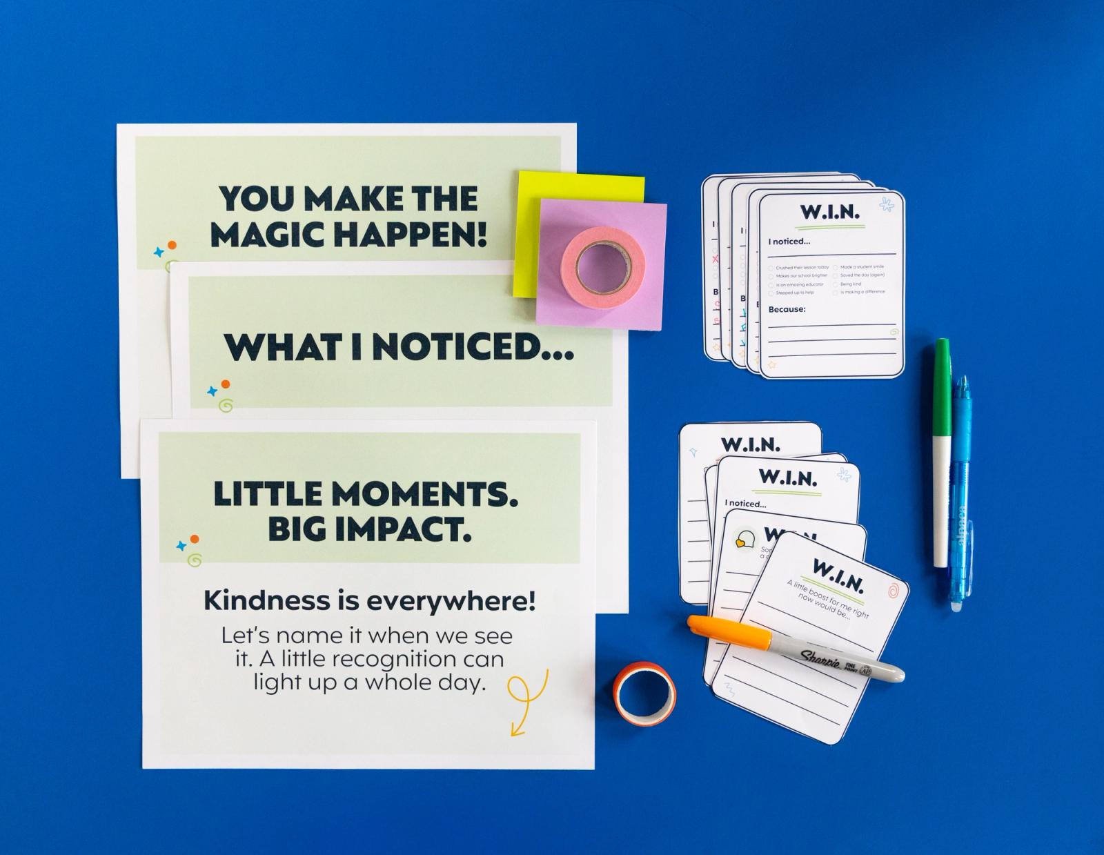 Three posters, notecards, and assorted office supplies lay on a dark blue background.