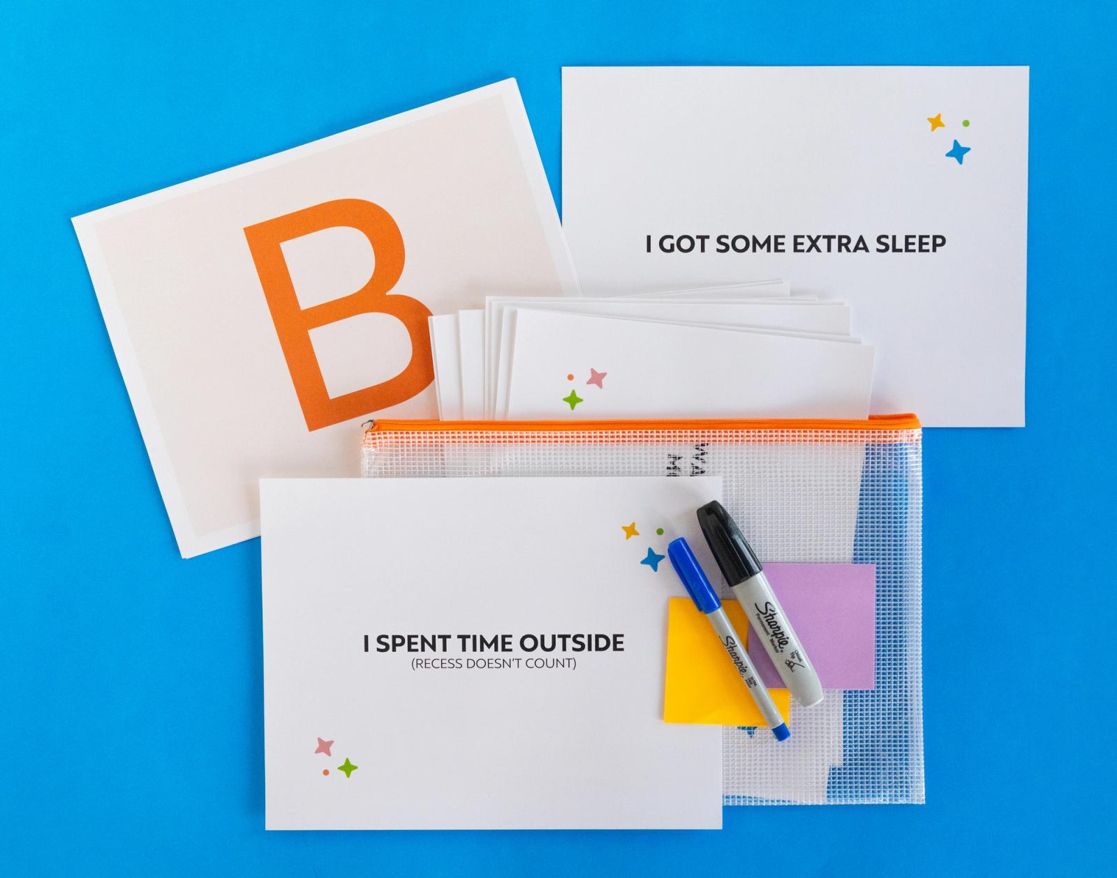 A sheet of paper with a large "B" on it, other sheets of paper, markers, and sticky notes lay on a blue background.