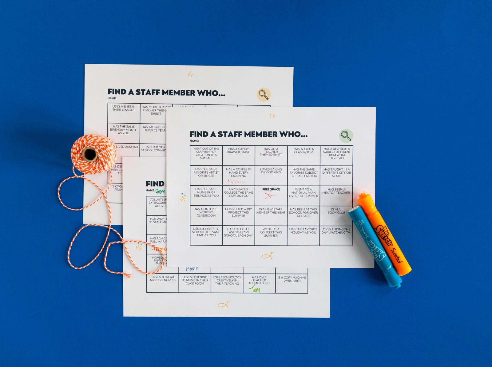 Three sheets of paper with bingo grids on them sit on a blue background. A spool of string and blue and orange highlights lay beside them.