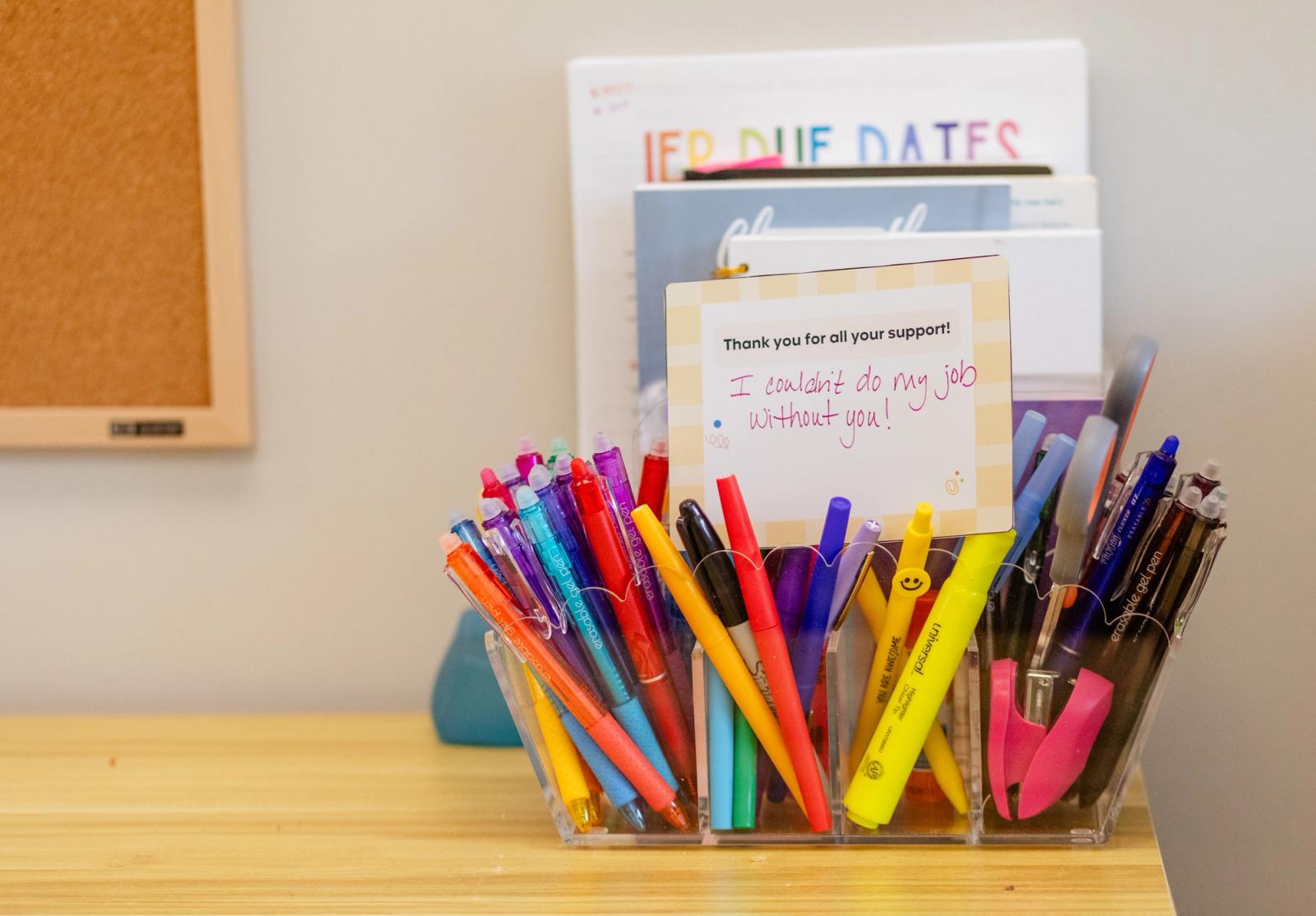 A hand-written note sits in a pencil and pen holders on a wooden desk.