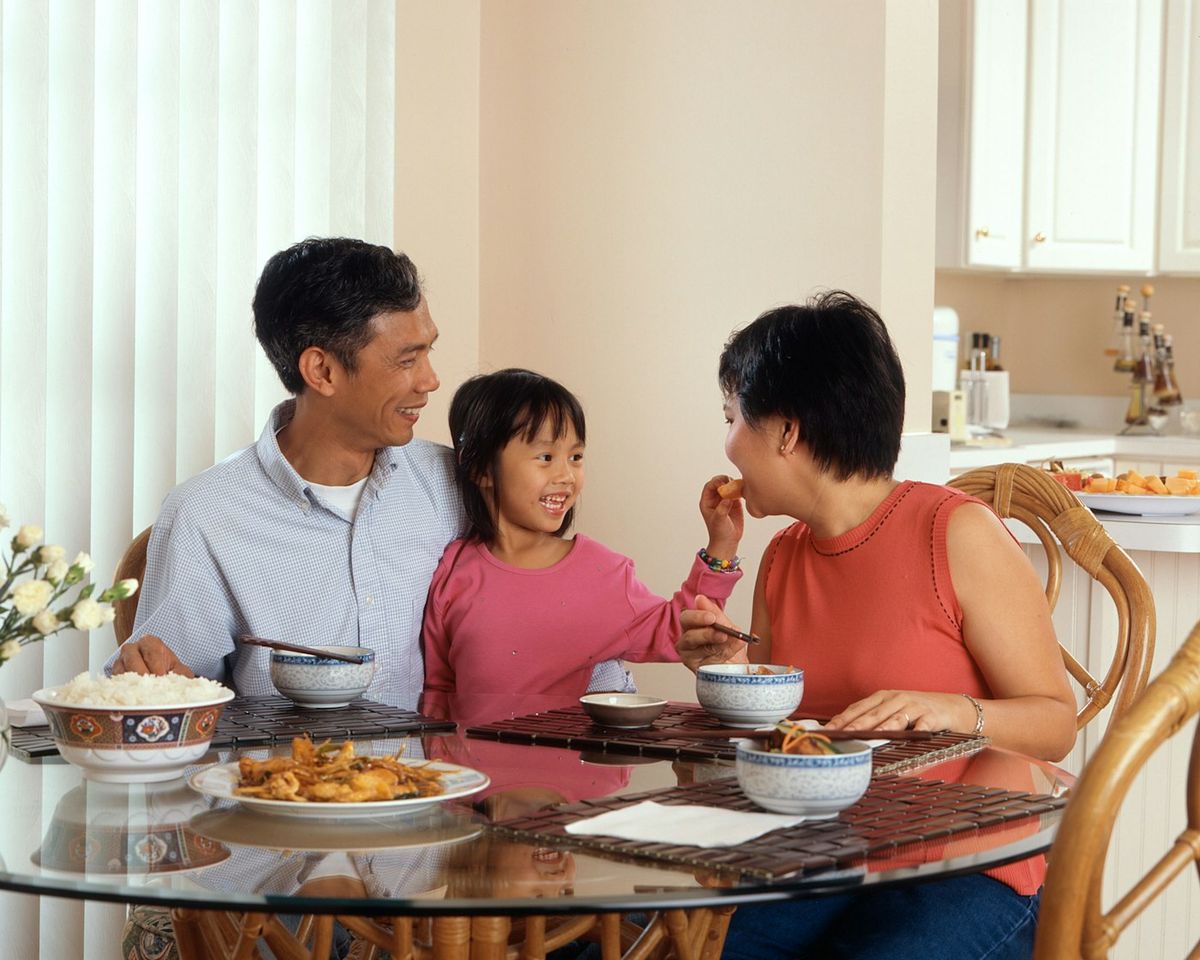 A family of three sitting at a dinner table sharing a meal from shared serving dishes placed in the middle, photo by National Cancer Institute on Unsplash