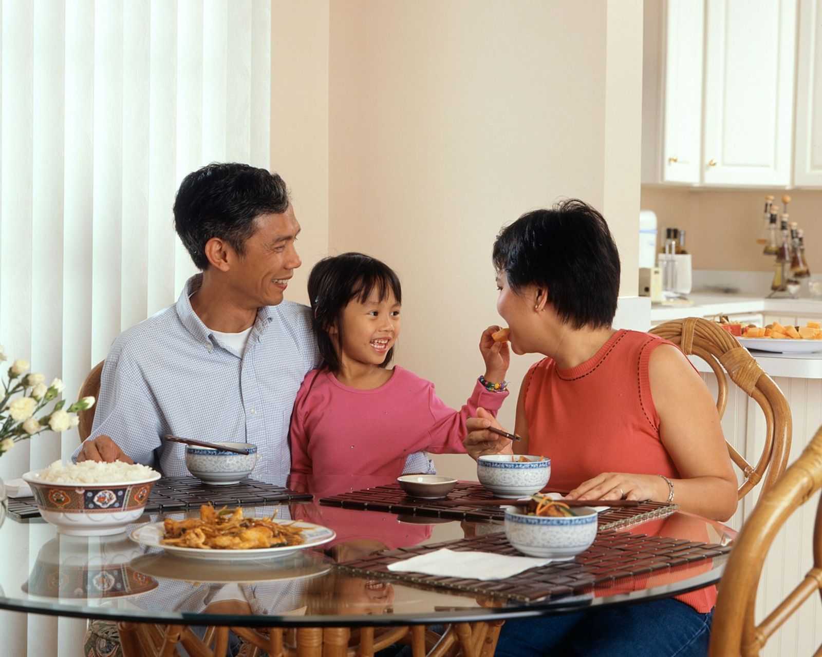 A family of three sitting at a dinner table sharing a meal from shared serving dishes placed in the middle, photo by National Cancer Institute on Unsplash