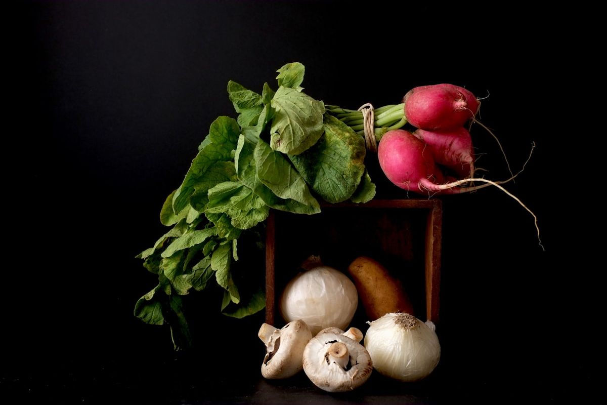 A wooden crate filled with fresh winter vegetables including pumpkin, carrots and leafy greens at an outdoor market, photo by Don Ricardo on Unsplash