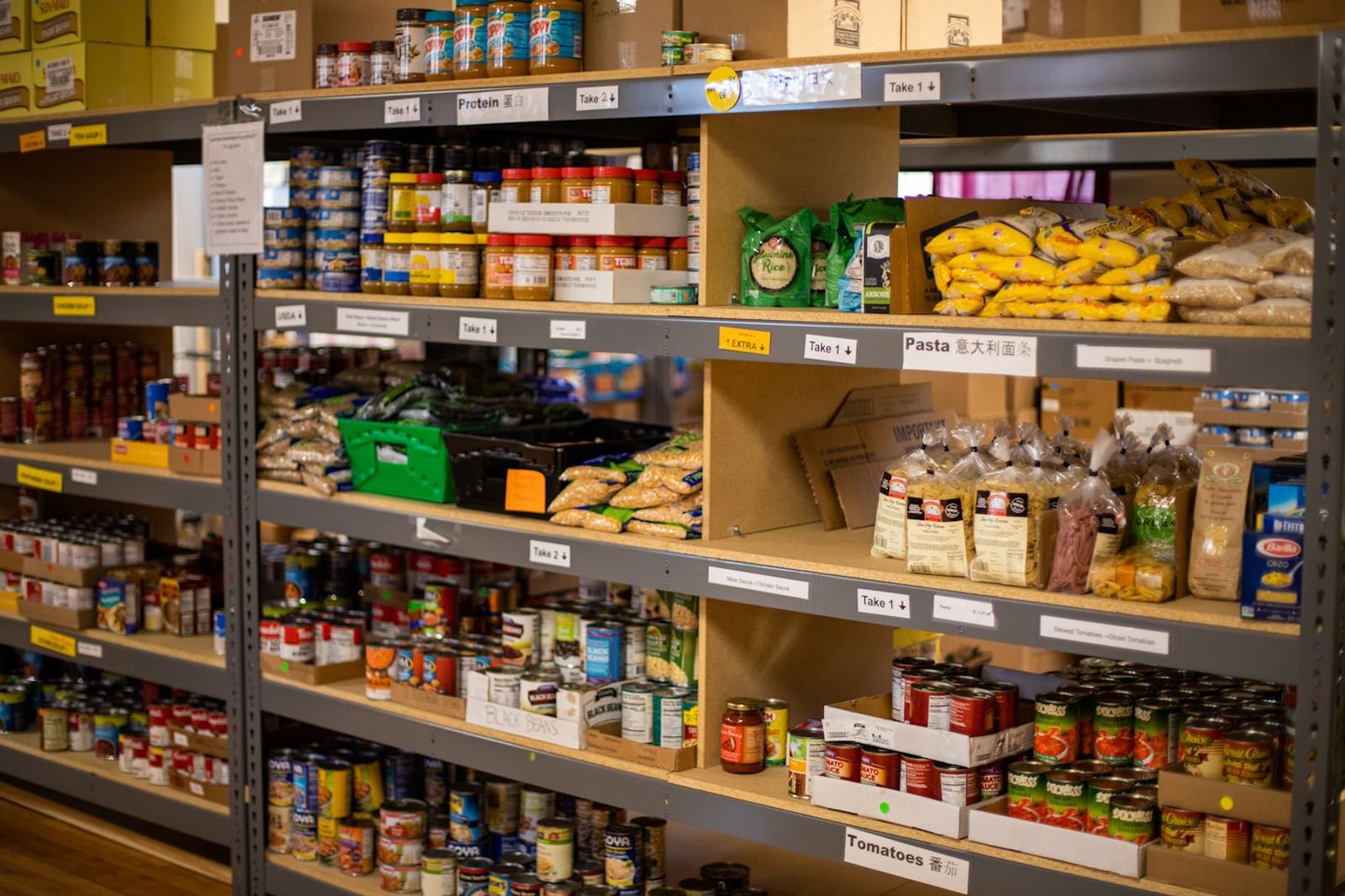 A shopping trolley filled with everyday pantry staples like tinned tomatoes, rice, pasta and vegetables in a supermarket aisle, photo by Aaron Doucett on Unsplash