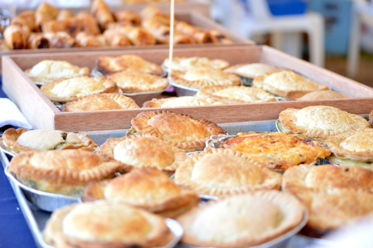 A golden pastry meat pie with tomato sauce sitting on a paper bag on a bakery counter, photo by FitNish Media on Unsplash