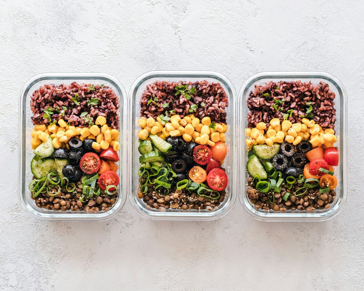 Several glass meal prep containers on a kitchen bench holding portions of mince, rice and roasted vegetables ready for the week ahead, photo by Ella Olsson on Unsplash