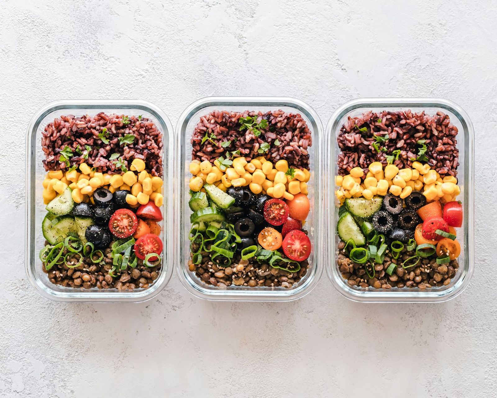 Several glass meal prep containers on a kitchen bench holding portions of mince, rice and roasted vegetables ready for the week ahead, photo by Ella Olsson on Unsplash