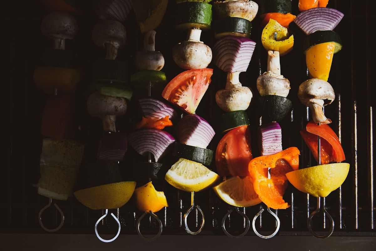 Corn, asparagus and capsicum charring on an outdoor barbecue grill alongside skewers, photo by Daniel Hooper 🌊 on Unsplash