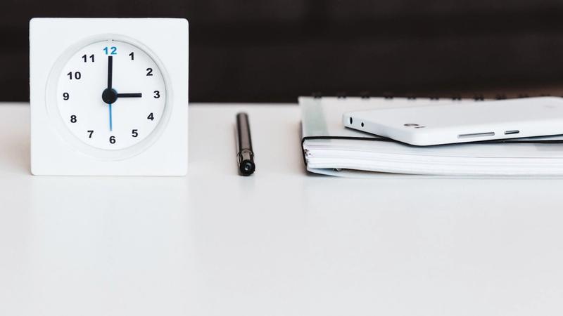 Clock on a desk with pen and notebook, representing the time cost of manual work