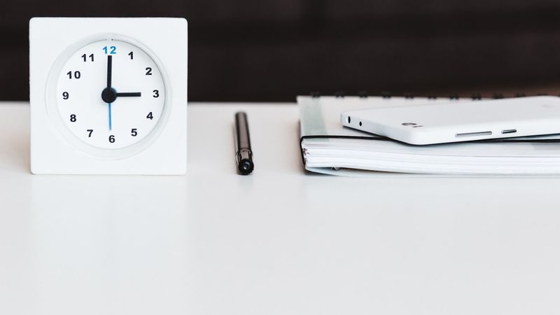 Clock on a desk with pen and notebook, representing the time cost of manual work