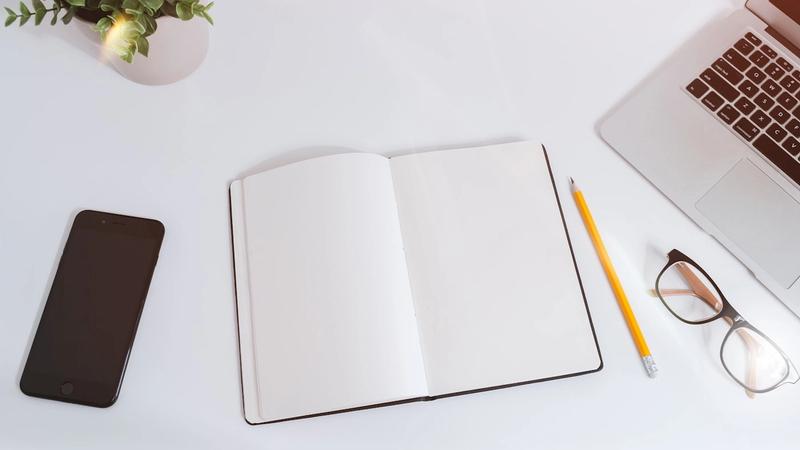 Open notebook on a desk beside a laptop, drafting a one page AI policy