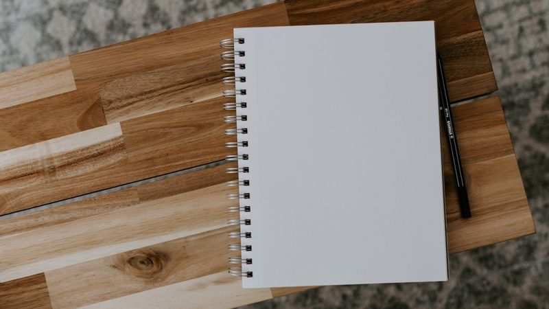 white spiral notebook on brown wooden table, photo by Kelly Sikkema on Unsplash