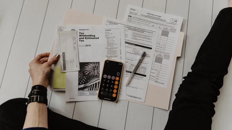 A person reviewing paperwork beside a pen and calculator, photo by Kelly Sikkema on Unsplash