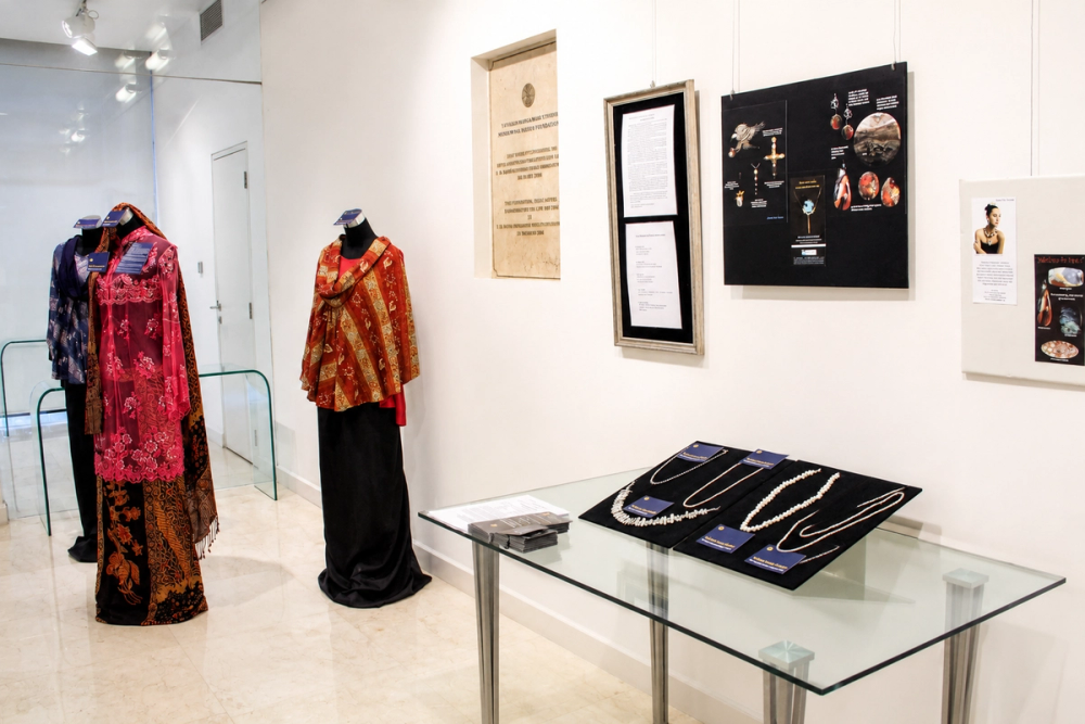 An exhibition in the Mawar Gallery, with garments on stands and jewellery in a glass display case