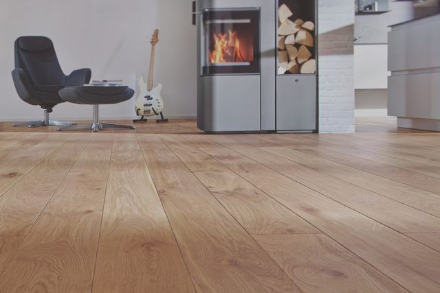 Lichte houten vloer in een woonkamer met zwarte fauteuil en ingebouwde haard