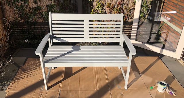Witte houten tuinbank op een terras, met verfblik en kwast ernaast
