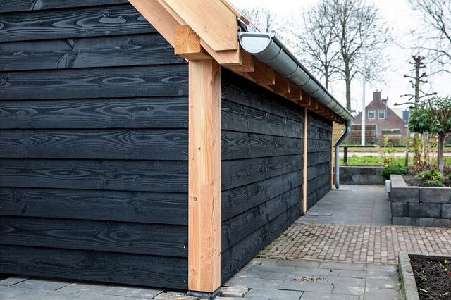 Zwart gebeitste houten schuur met overkapping in een tuin