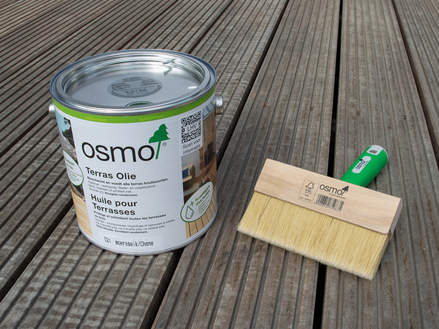 Blik Osmo-beits met kwast op een vergrijsd houten terras