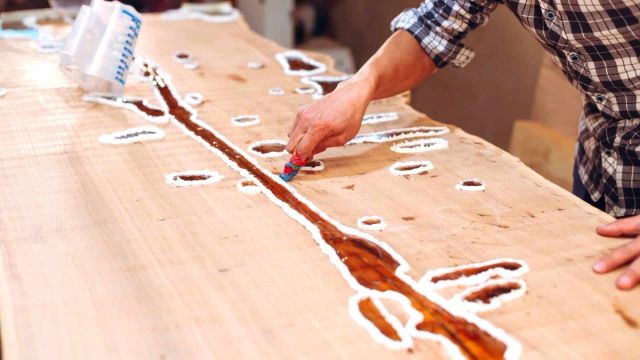 Twee mensen brengen epoxy aan op een houten tafelblad