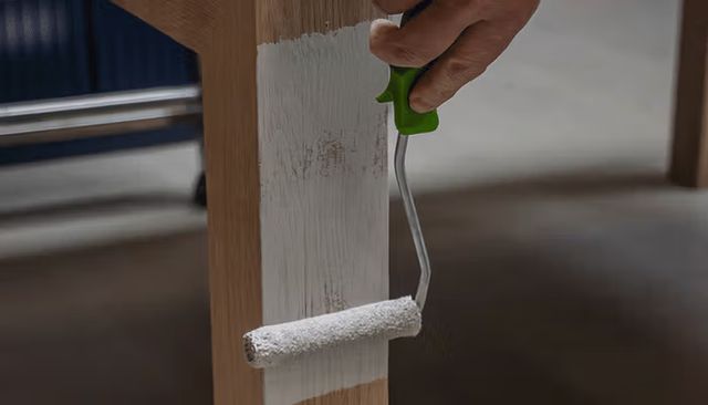Hand die met een verfroller een houten kast wit verft