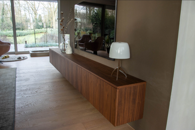 Donker houten dressoir tegen een lichte wand met lamp