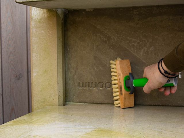 Hand die met een borstel groene aanslag van een tegelvloer schrobt