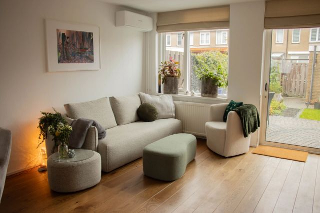 Woonkamer met vurenhouten vloer, lichte bank en uitzicht op de tuin