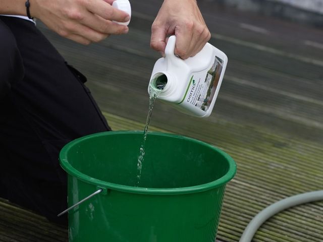 Hand die reinigingsmiddel in een groene emmer giet bij tuinmeubelen