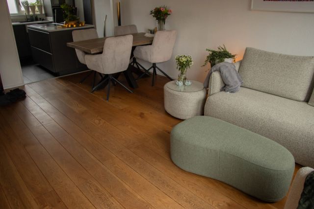 Woonkamer met geoliede houten vloer, lichte bank en poef