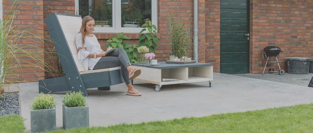 Vrouw op een houten loungestoel op een terras bij een woning