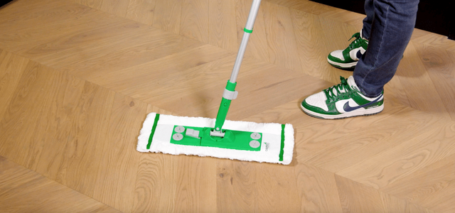 Persoon die met een vlakmop een visgraat houten vloer behandelt