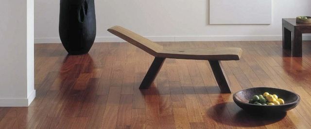 Donkere jatoba houten vloer met een houten ligbank en zwarte vaas