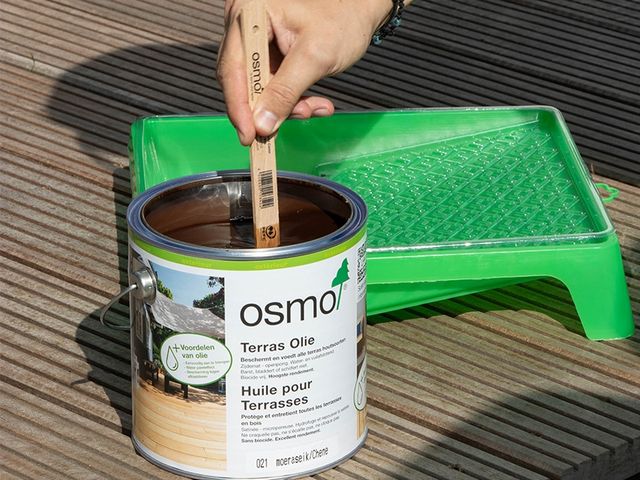 Hand roert in een blik Osmo Terras-Olie boven een groene verfbak