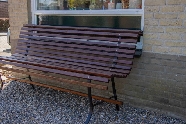 Donkerrode houten tuinbank op grind