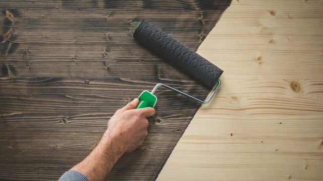 Hand die met een verfroller een houten plank zwart verft