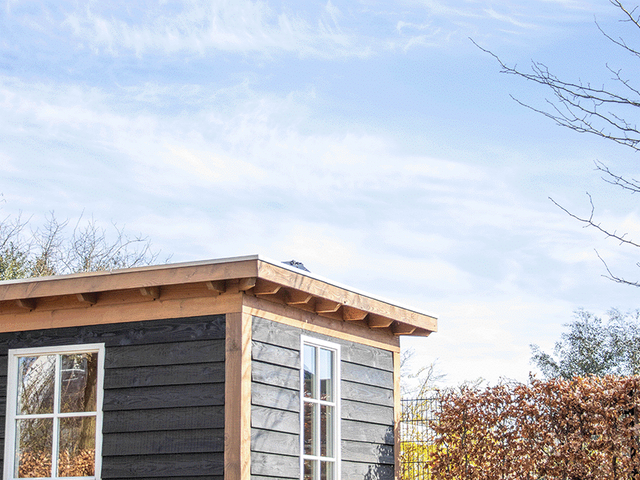 Zwart tuinhuis met wit kozijn onder een blauwe lucht