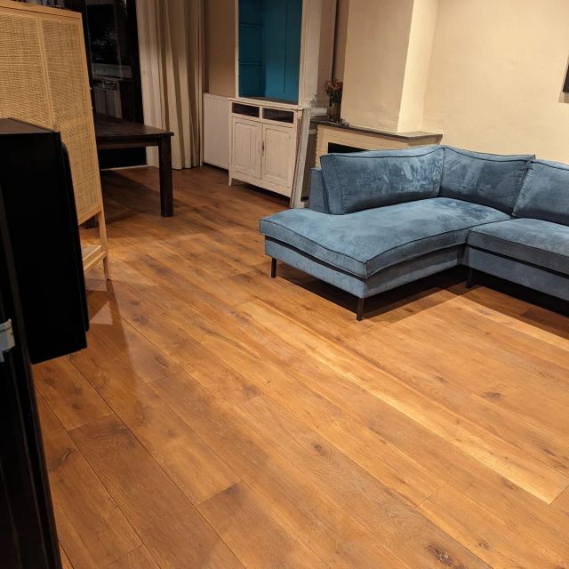 Eiken vloer in de woonkamer met blauwe hoekbank, behandeld met Osmo Hardwax-Olie Farbig 3072, Amber