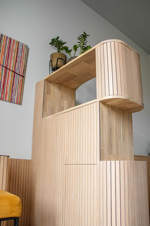 Lichte houten kast met ronde vormen tegen een witte wand