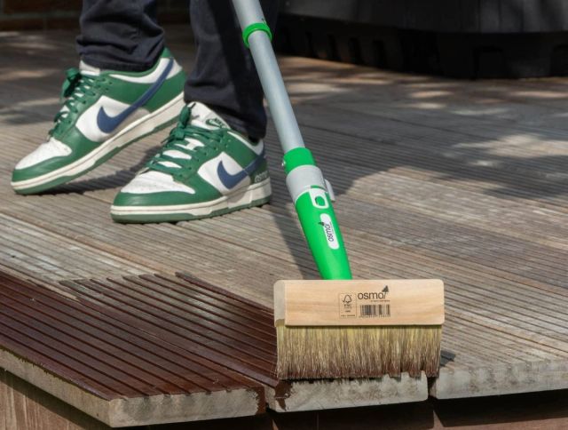Persoon die met een blokkwast aan een steel een terras beitst