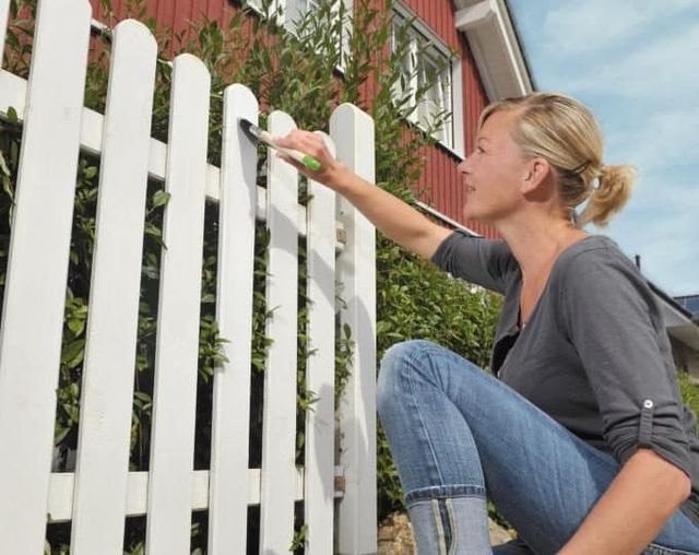 Vrouw die een witte houten tuinpoort beitst