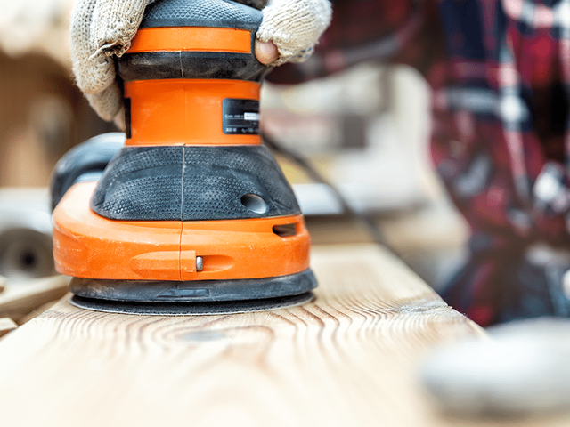Handen met een schuurmachine op een houten plank