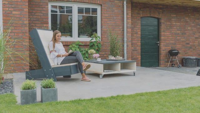 Vrouw op een houten loungestoel op een terras bij een woning