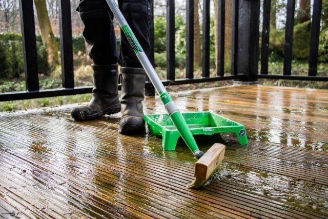 Persoon die met een schrobborstel een bankirai terras reinigt