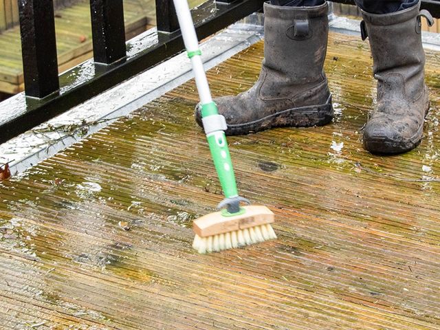 Persoon met laarzen die met een schrobber een houten balkonvloer reinigt
