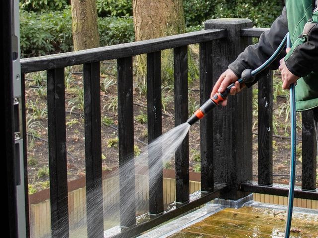 Persoon die met een hogedrukspuit een houten balkonhek reinigt