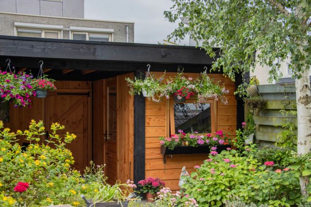 Donker gebeitst tuinhuis met bloeiende planten ervoor